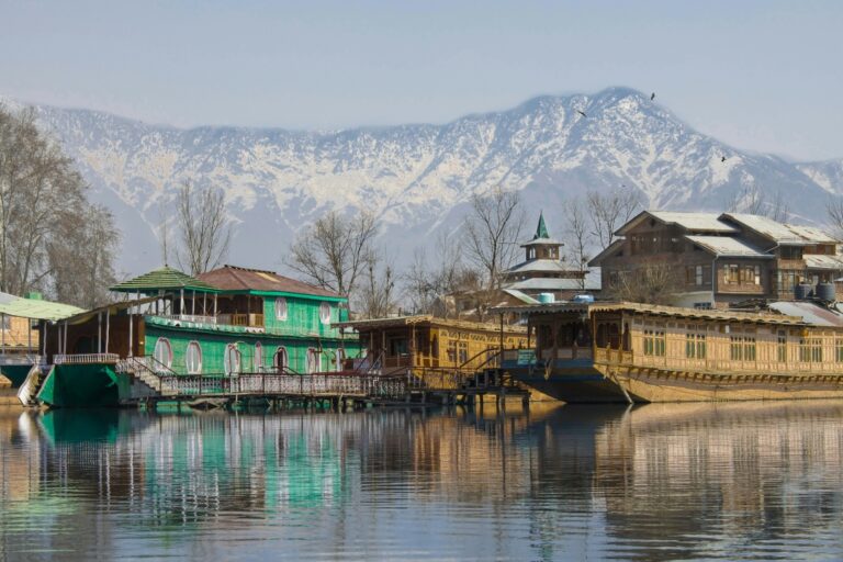 Traditional houseboat on Dal Lake, featuring intricate wooden carvings and vibrant colors, moored amidst serene waters with stunning reflections of the surrounding mountains and lush trees, creating a picturesque and tranquil scene