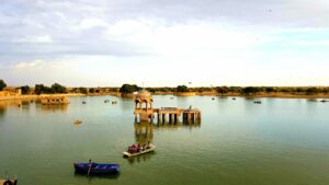 Tourists enjoying a peaceful boat ride on Gadisar Lake, with the serene water and surrounding architecture in the background