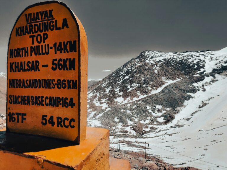 Snow-covered Khardung La Pass, one of the highest motorable roads in the world, with rugged mountain landscapes and a signboard marking its elevation at 17,582 feet in Leh Ladakh