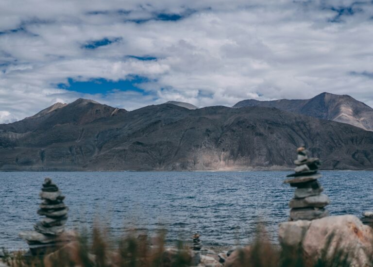 Close-up of Pangong Tso Lake's crystal-clear waters, reflecting the surrounding snow-capped peaks and bright sky.