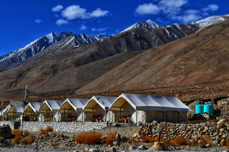 Camping tents near the shores of Pangong Tso, reflecting the snow-capped peaks in the crystal-clear lake water at dawn