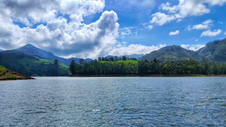 "Scenic view of Mattupetty Dam in Kerala, surrounded by lush green hills and reflecting the blue sky in its calm waters.