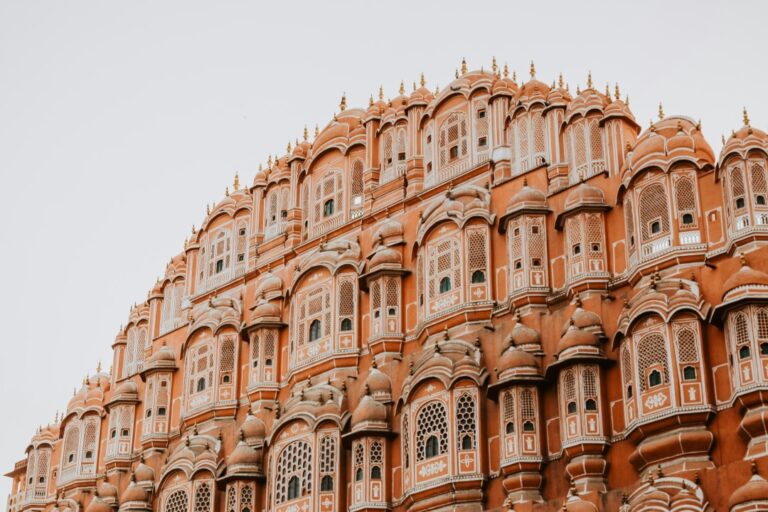 The intricate facade of Hawa Mahal in Jaipur, India, featuring numerous small windows and delicate latticework in warm red and pink sandstone.